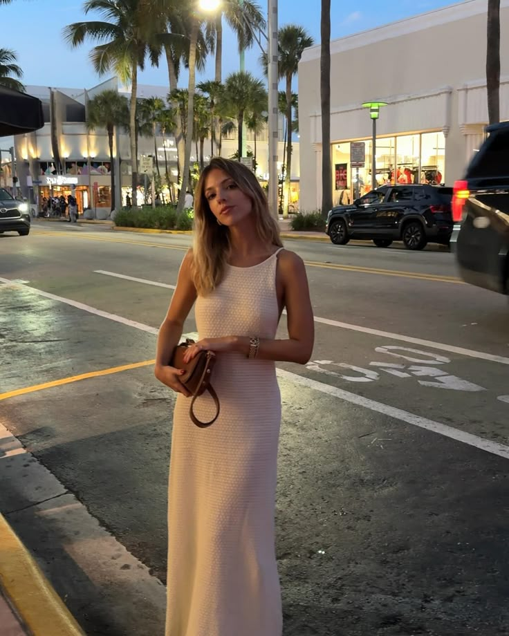 a woman in a white dress is standing on the street with her handbag and purse