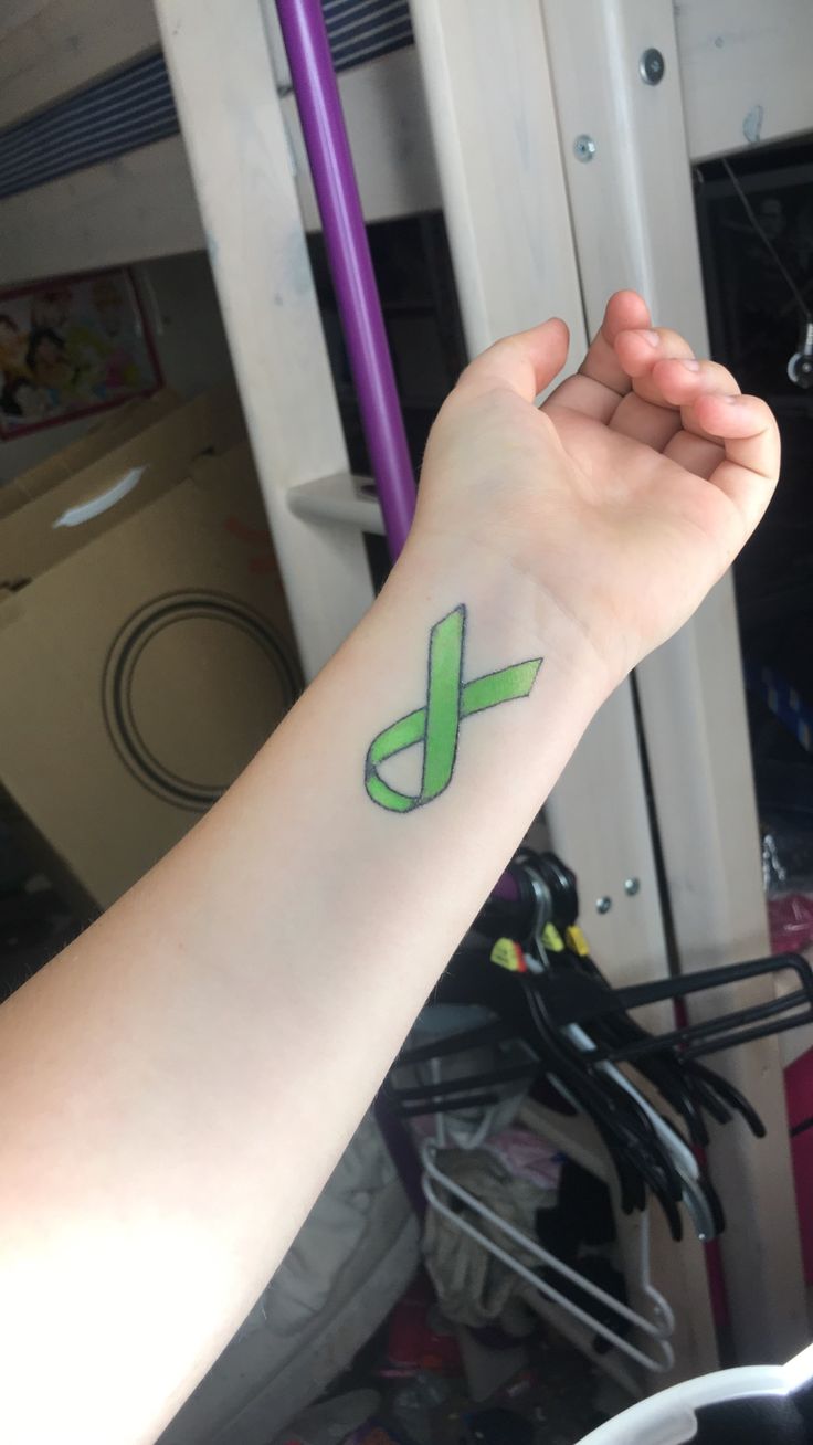 a person's arm with a green ribbon tattoo on the left side of their arm