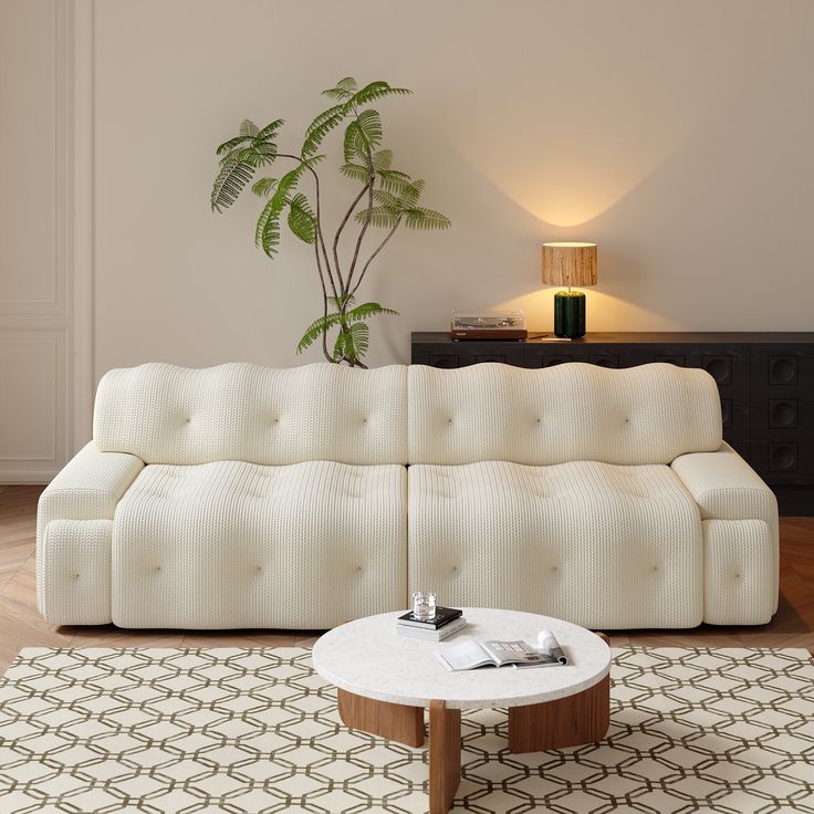 a white couch sitting on top of a wooden table in a living room next to a potted plant