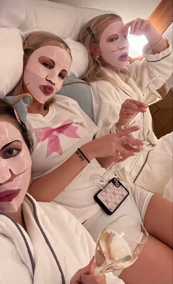 three women in white shirts laying on a bed with their faces painted to look like they are holding wine glasses