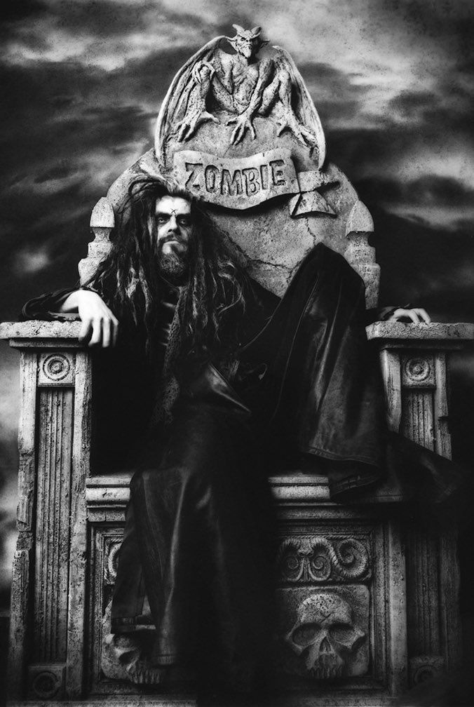 a black and white photo of a man with long hair sitting on a bench in front of a statue