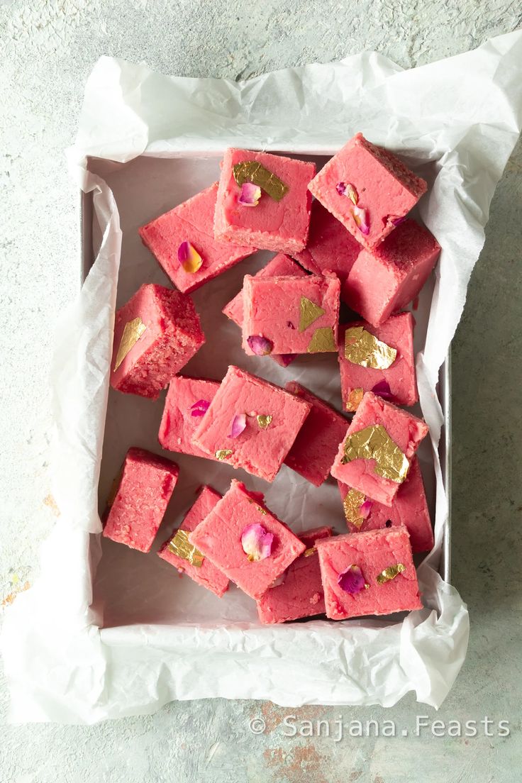 there are many pieces of pink and gold cake in the box on the table, ready to be eaten