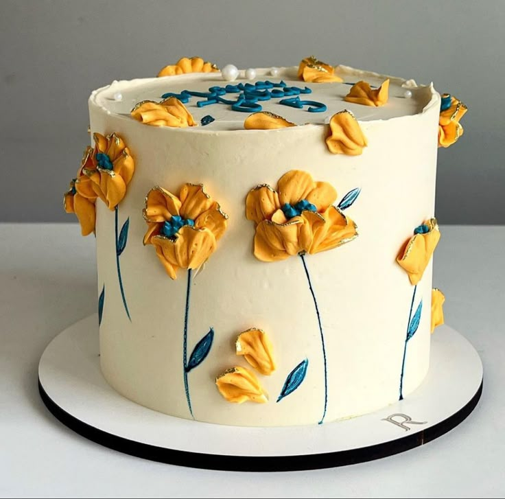 a white cake decorated with yellow flowers and blue icing on a plate in front of a gray background