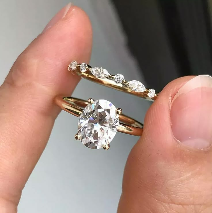 a person holding an engagement ring with a diamond in it's middle and two wedding bands on their fingers