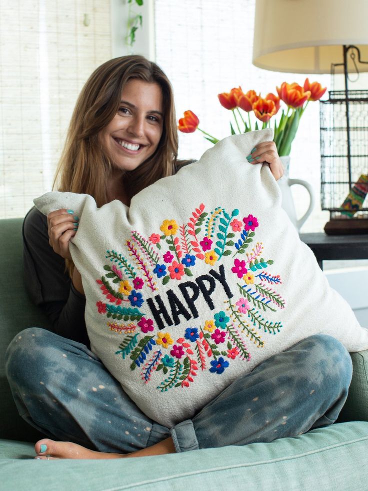 a woman sitting on a couch holding a pillow with the words happy printed on it