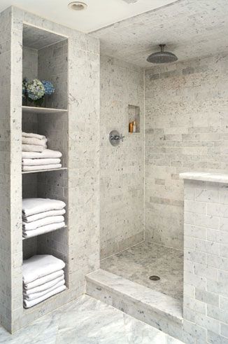 a bathroom with white towels stacked on the shelves and a shower in the back ground