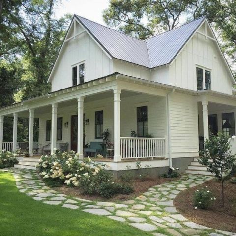 a white house with porches and flowers on the front lawn