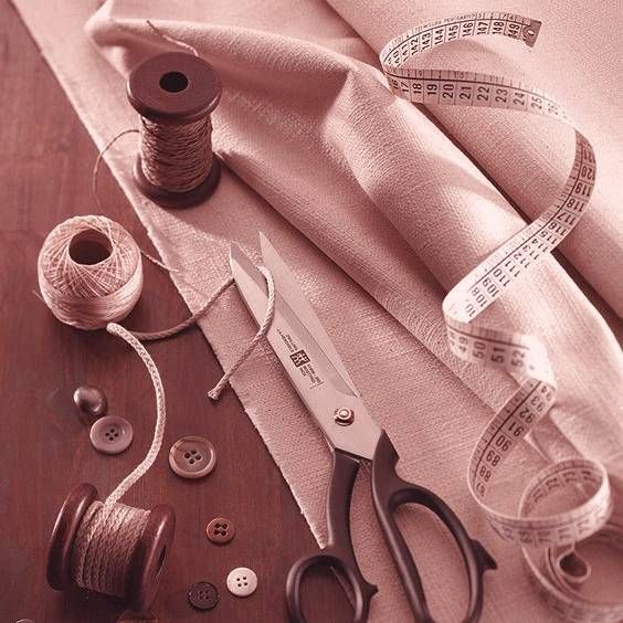 scissors, thread, measuring tape and other crafting supplies on a table with pink hued background