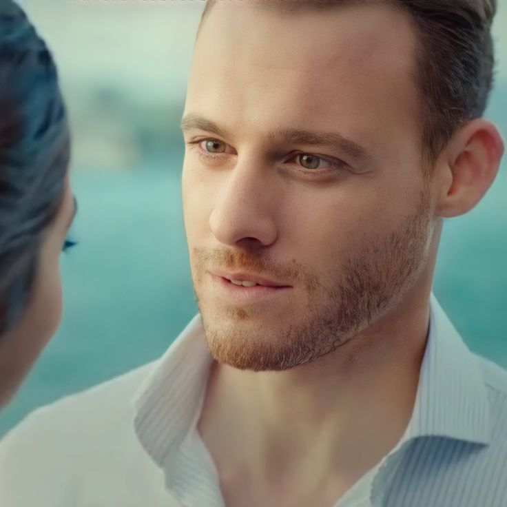 a man and woman looking at each other in front of the camera with water behind them