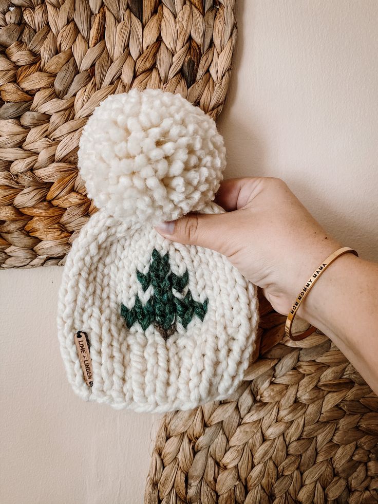 a hand holding a white knitted hat with green leaves on the front and side