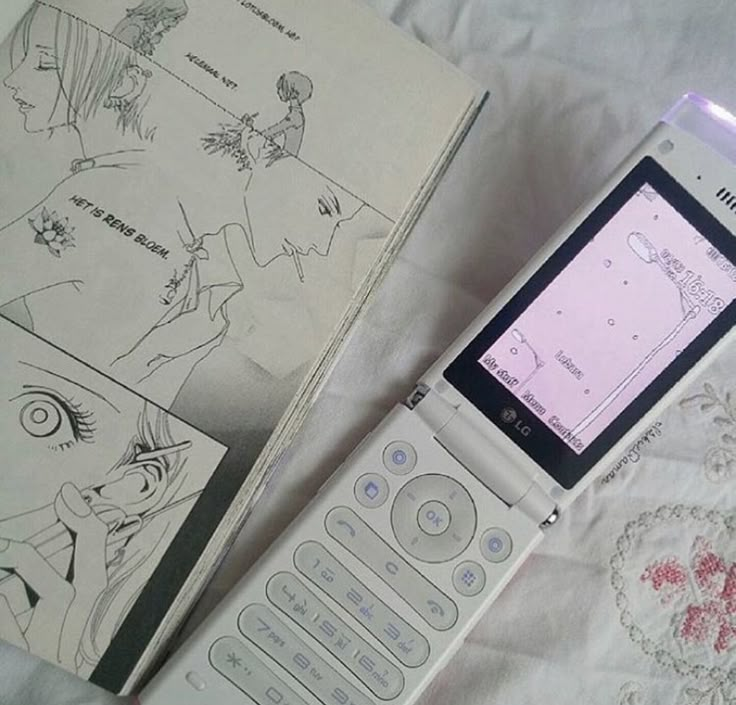 an old cell phone sitting on top of a table next to a book and pen