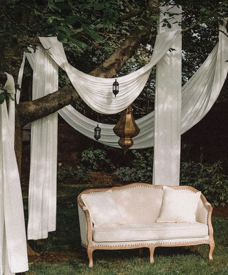 a white couch sitting in the middle of a lush green field next to a tree