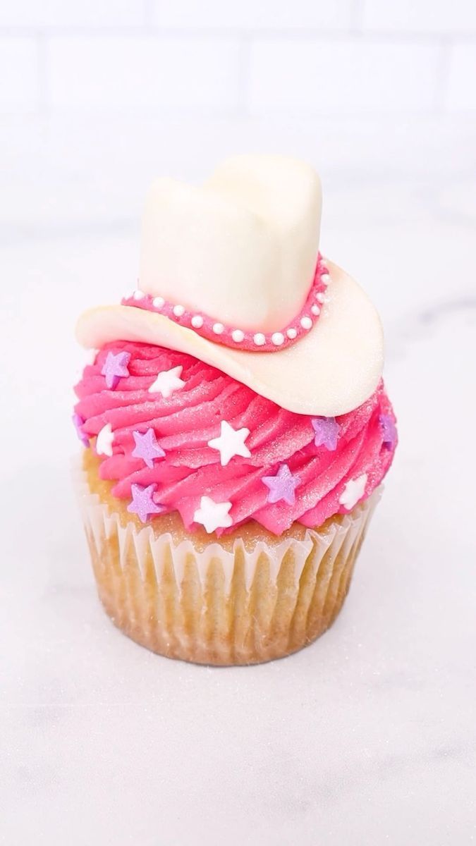 a cupcake with pink frosting and a white cowboy hat on it's top