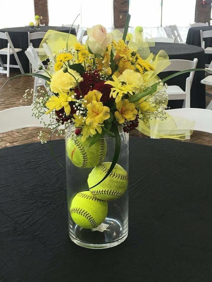 a vase filled with yellow flowers and baseballs sitting on top of a black table