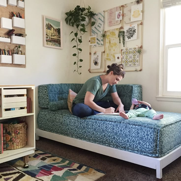 a woman sitting on top of a blue couch in a living room next to a window