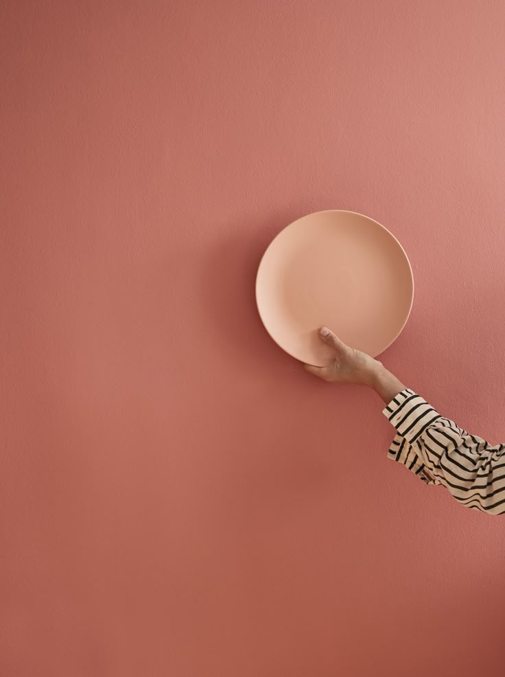 a woman holding a plate in front of a pink wall