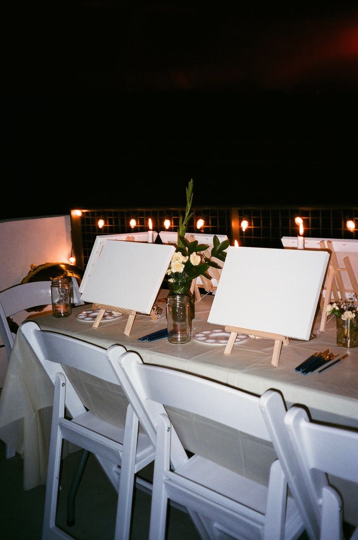 there is a table set up with white chairs and flowers in vases on it