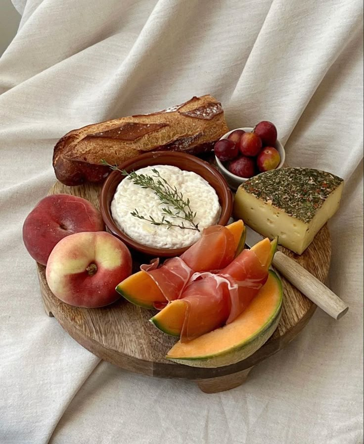 a wooden platter filled with different types of cheeses and fruit on top of a white sheet