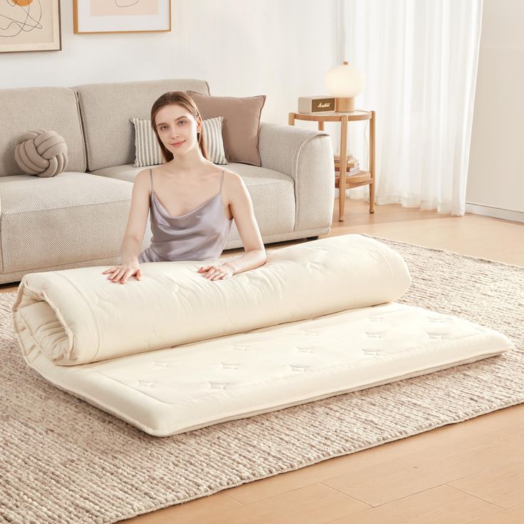 a woman sitting on top of a mattress in front of a couch with a pillow