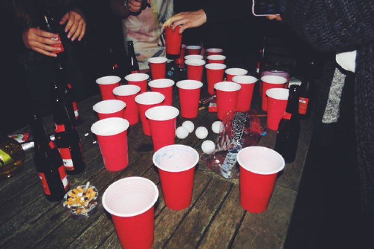 red cups are lined up on a wooden table with people standing around and eating food