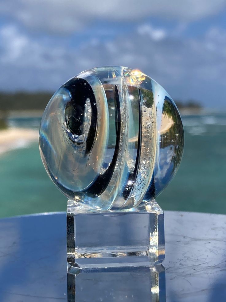 a clear glass object sitting on top of a blue table next to the ocean and sky