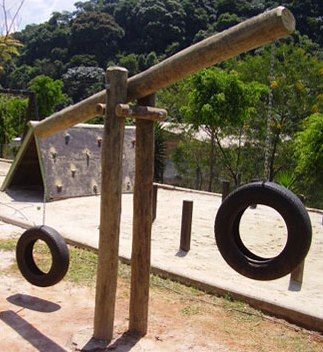 an outdoor play area with tire swings and wooden posts in the foreground, surrounded by trees