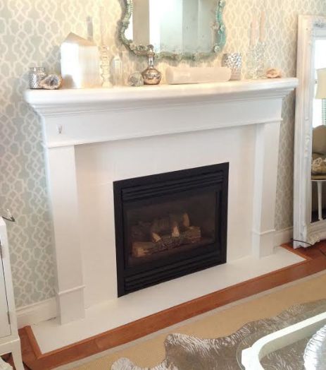 a living room with a fire place and mirror on the fireplace mantel, in front of a wallpapered background