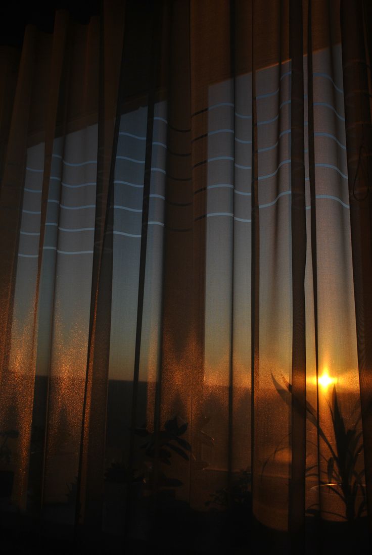 the sun is setting behind sheer curtains