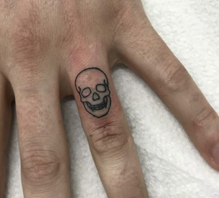 a person with a skull tattoo on their ring finger and the other hand is showing