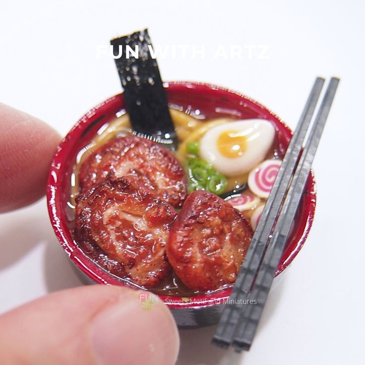 a miniature bowl of food with chopsticks and an egg in it is being held by a hand