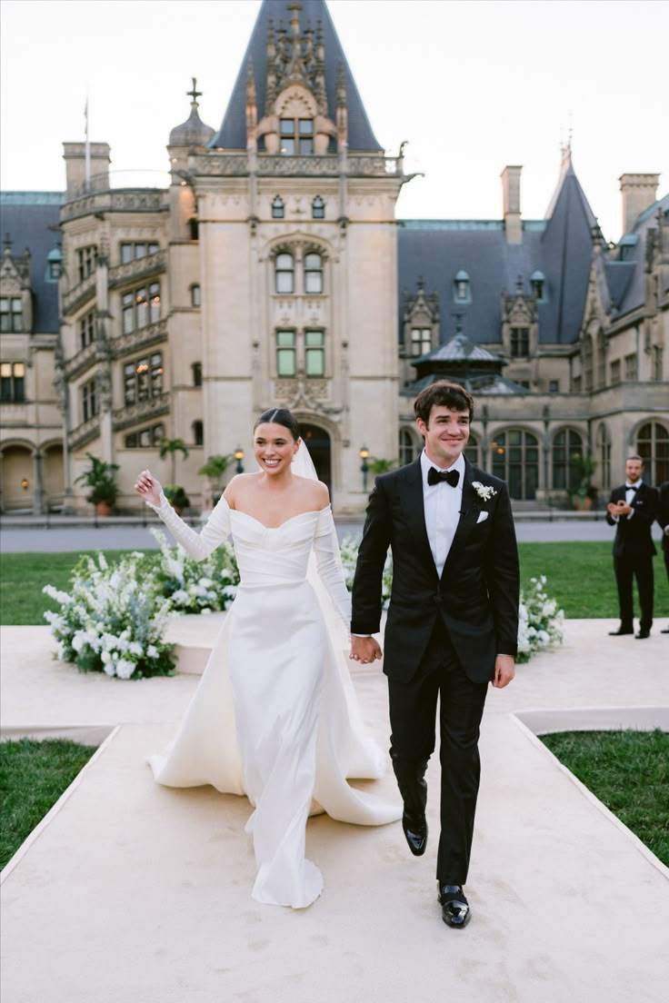 a bride and groom walking down the aisle in front of an old castle like building