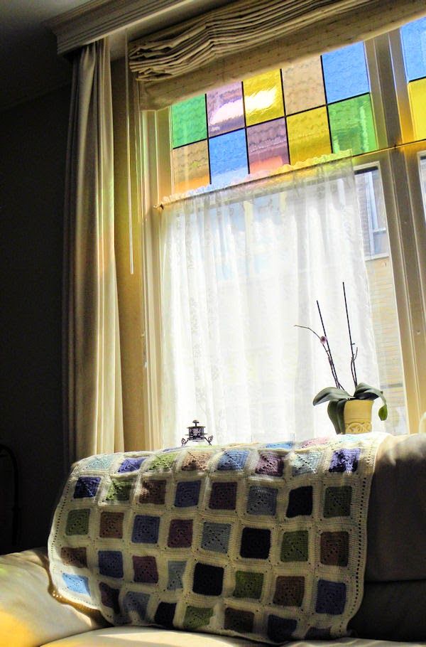 a couch with a blanket on top of it next to a window covered in multicolored squares