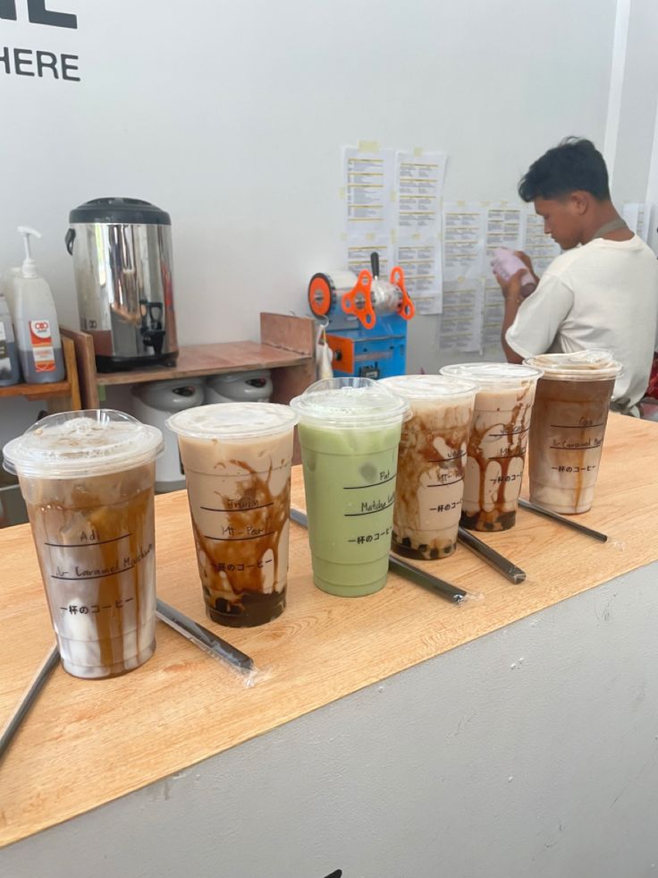 there are many cups on the counter with different drinks in each cup and one has a spoon