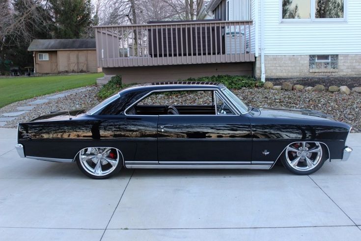 an old black car parked in front of a house with white trim and chrome rims