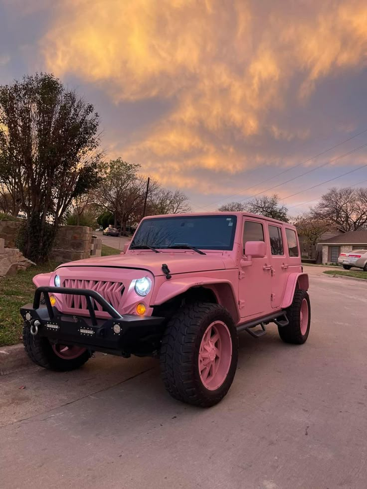 a pink jeep parked on the side of a road in front of a house at sunset