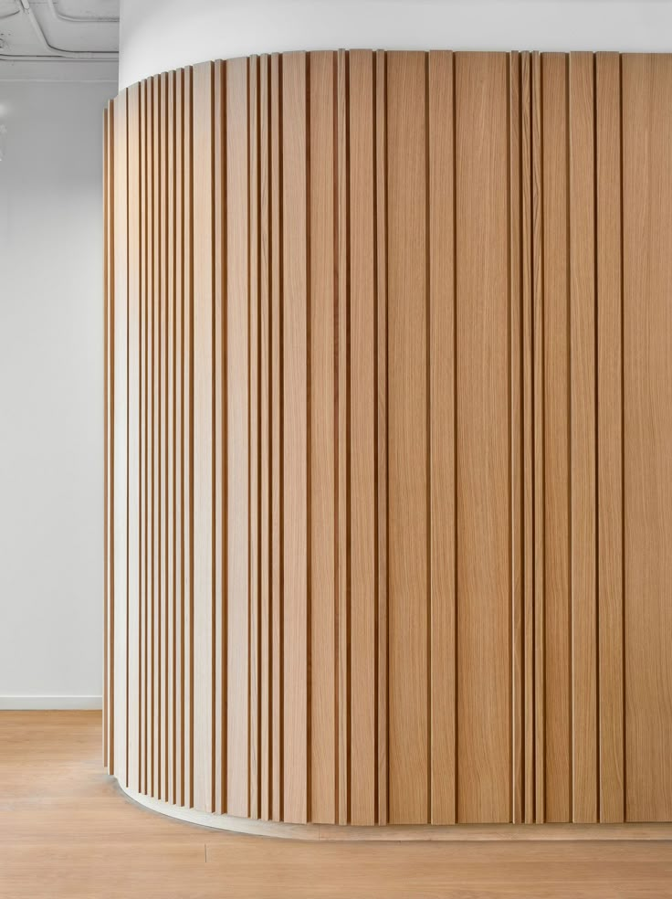 an empty room with wooden slats on the wall and wood flooring in front of it