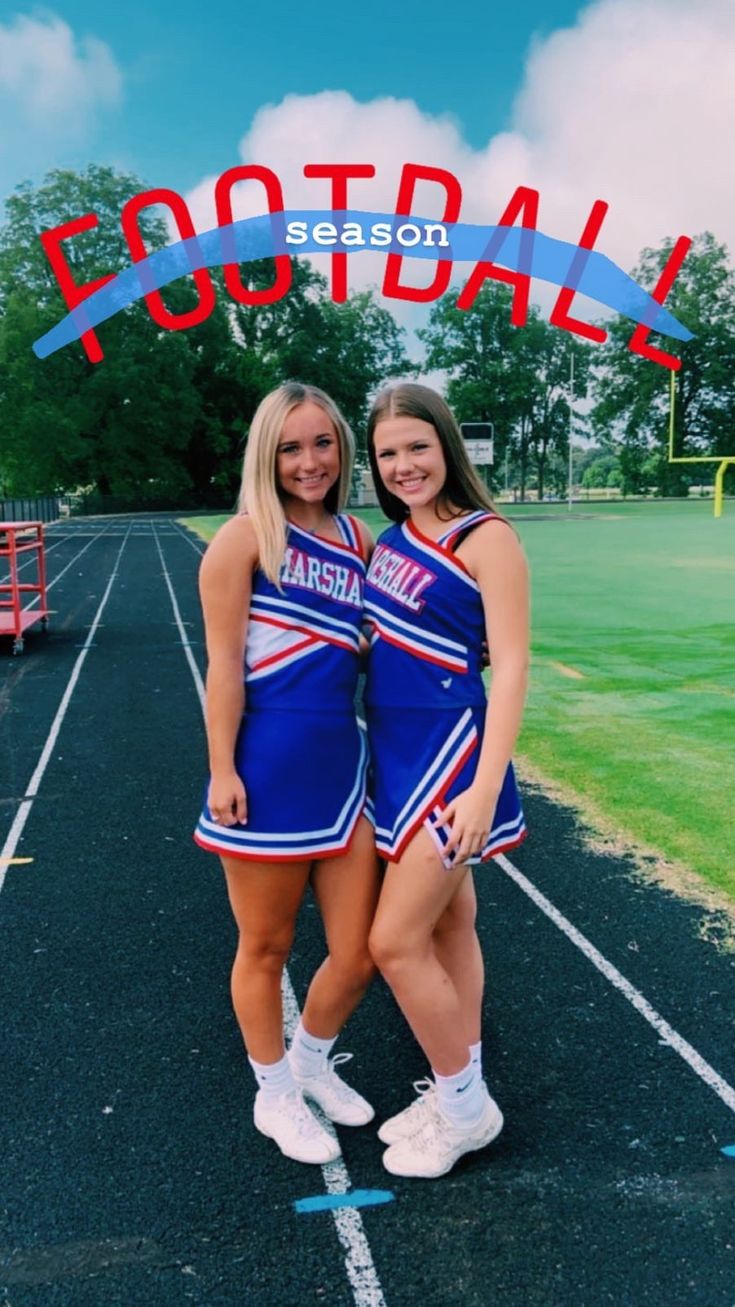 two cheerleaders pose for a photo in front of the football stadium sign that says football season