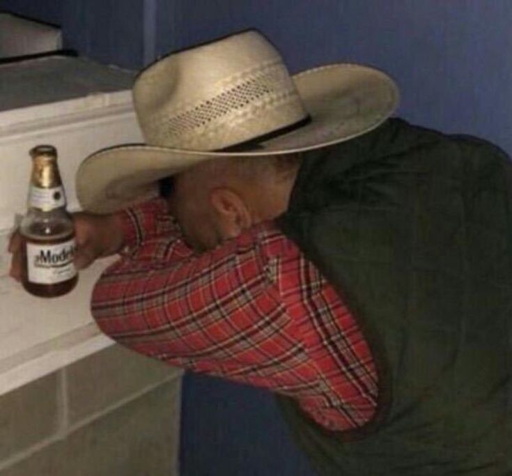 a man wearing a cowboy hat leaning against a wall with a bottle in his hand