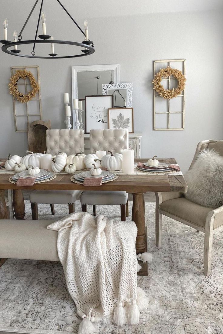 the dining room table is set with white pumpkins, candles and wreaths on it