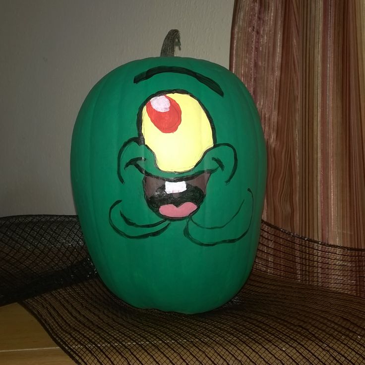 a green pumpkin with an evil face painted on it's side sitting on a table