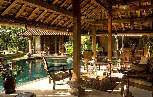 an outdoor living area next to a pool with chairs and tables on the patio, surrounded by greenery