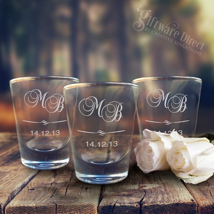 three personalized shot glasses sitting on top of a wooden table next to white roses