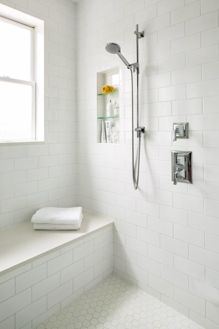 a white tiled bathroom with a window and shower head