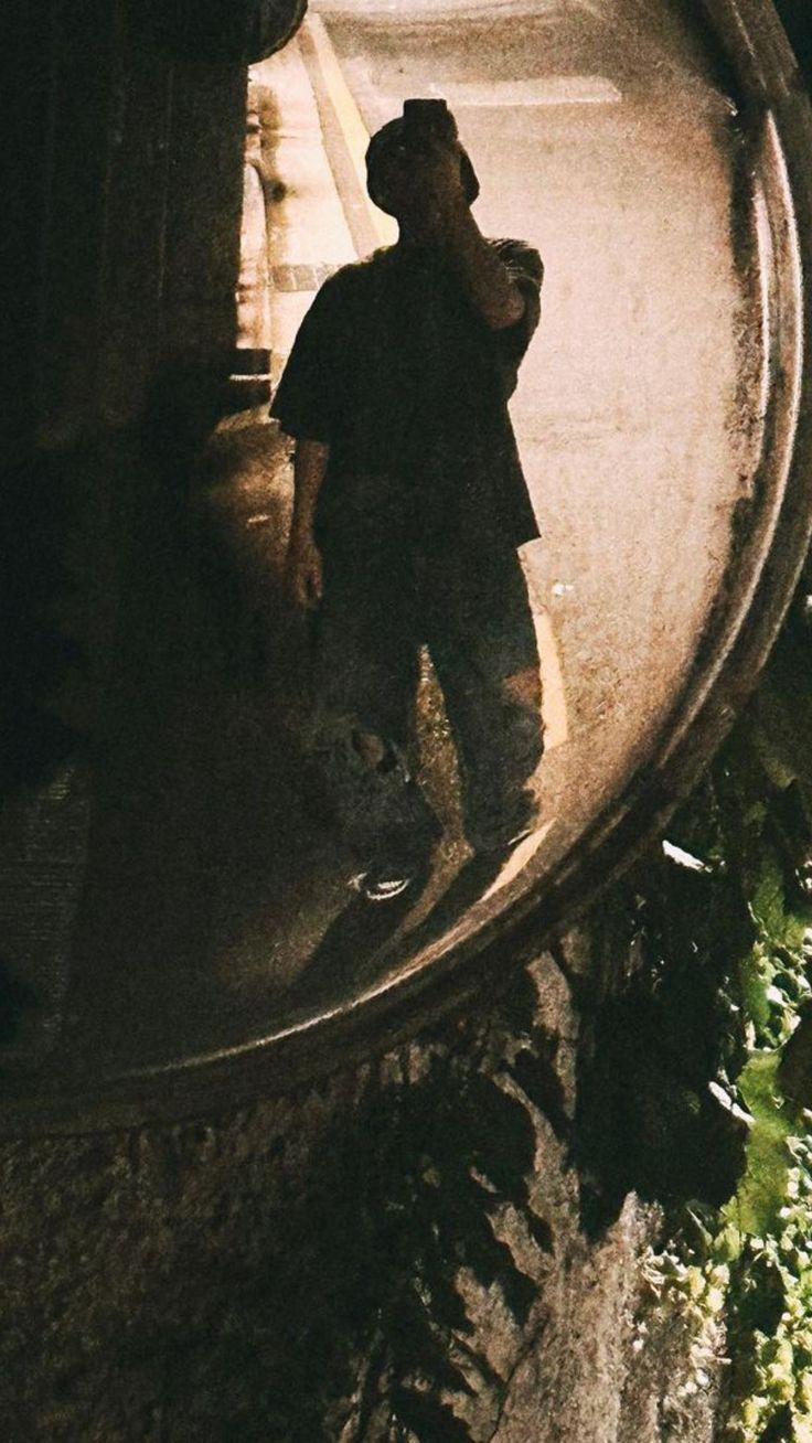 a man standing in front of a mirror on the side of a building at night