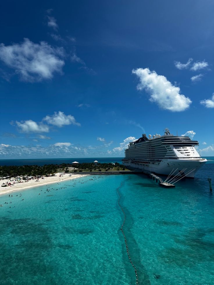 a cruise ship docked at the beach with clear blue water and people swimming in the ocean