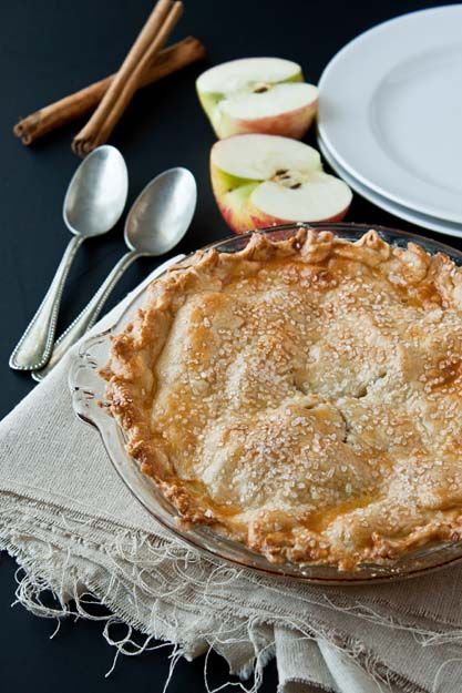 an apple pie sitting on top of a table next to plates and spoons with apples in the background