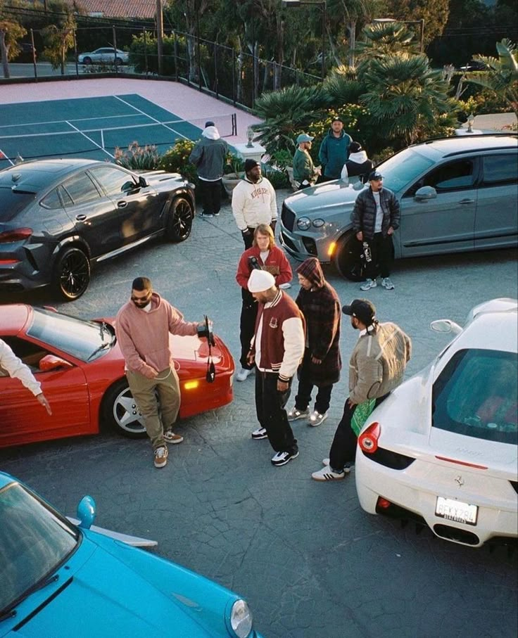 a group of people standing in the middle of a parking lot next to parked cars