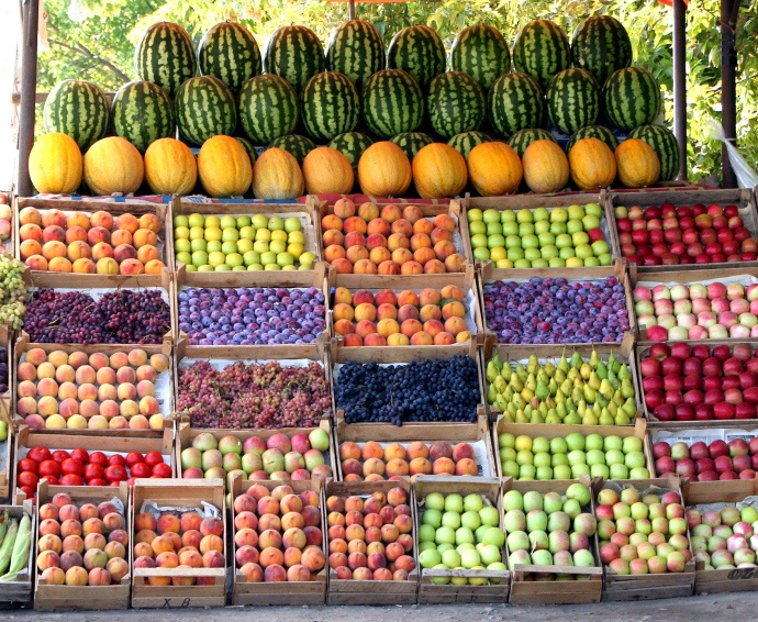 many different types of fruits and vegetables on display at a fruit stand in front of trees