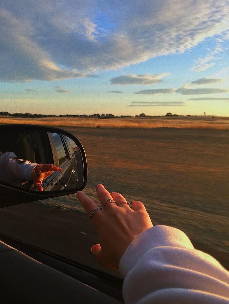 a woman's hand on the side mirror of a car as she drives through an open field