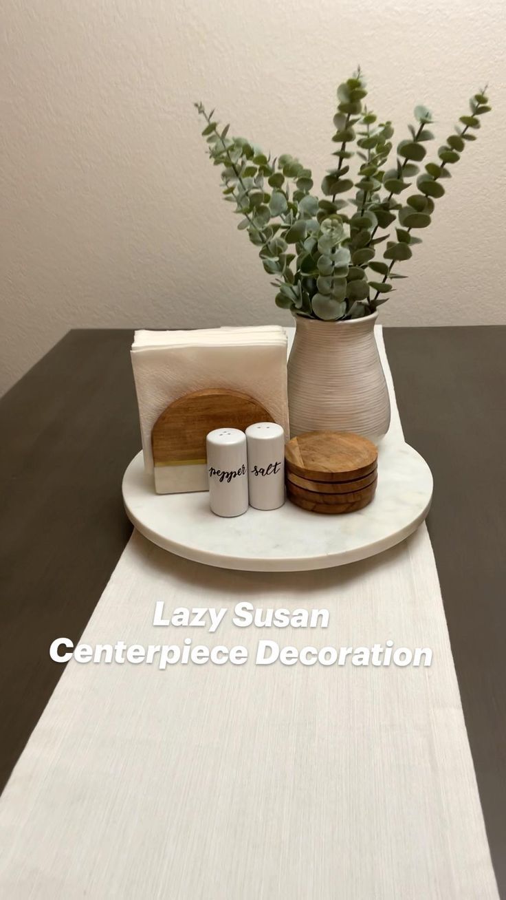 a white plate topped with two cups and a vase filled with green plants next to each other